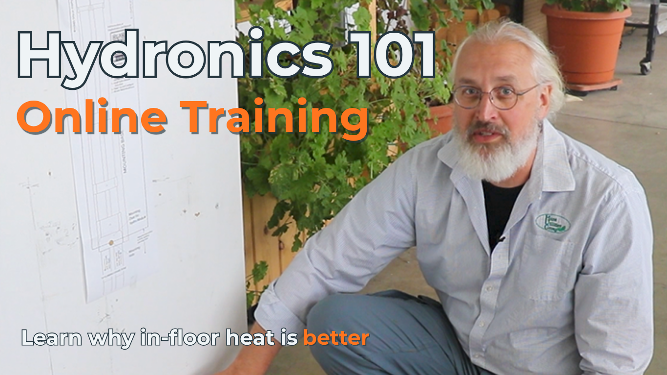 A man with glasses, a white beard, and a light blue button-up shirt kneels beside a white board with technical drawings. Large text reads 'Hydronics 101 Online Training' and 'Learn why in-floor heat is better.